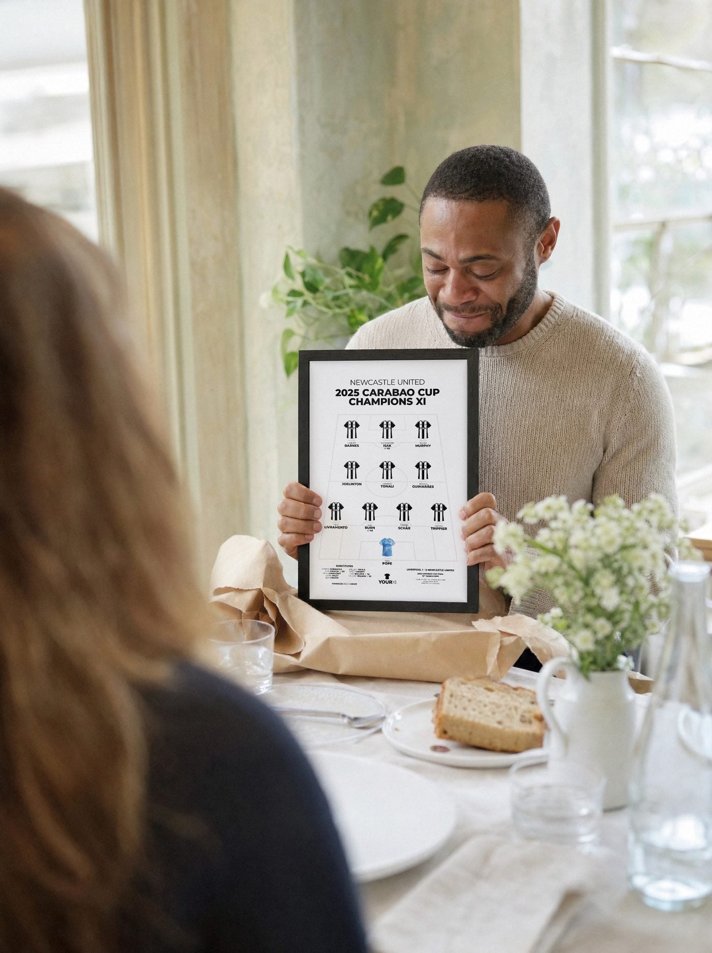 A man unwraps a framed Newcastle United XI print at a lunch table