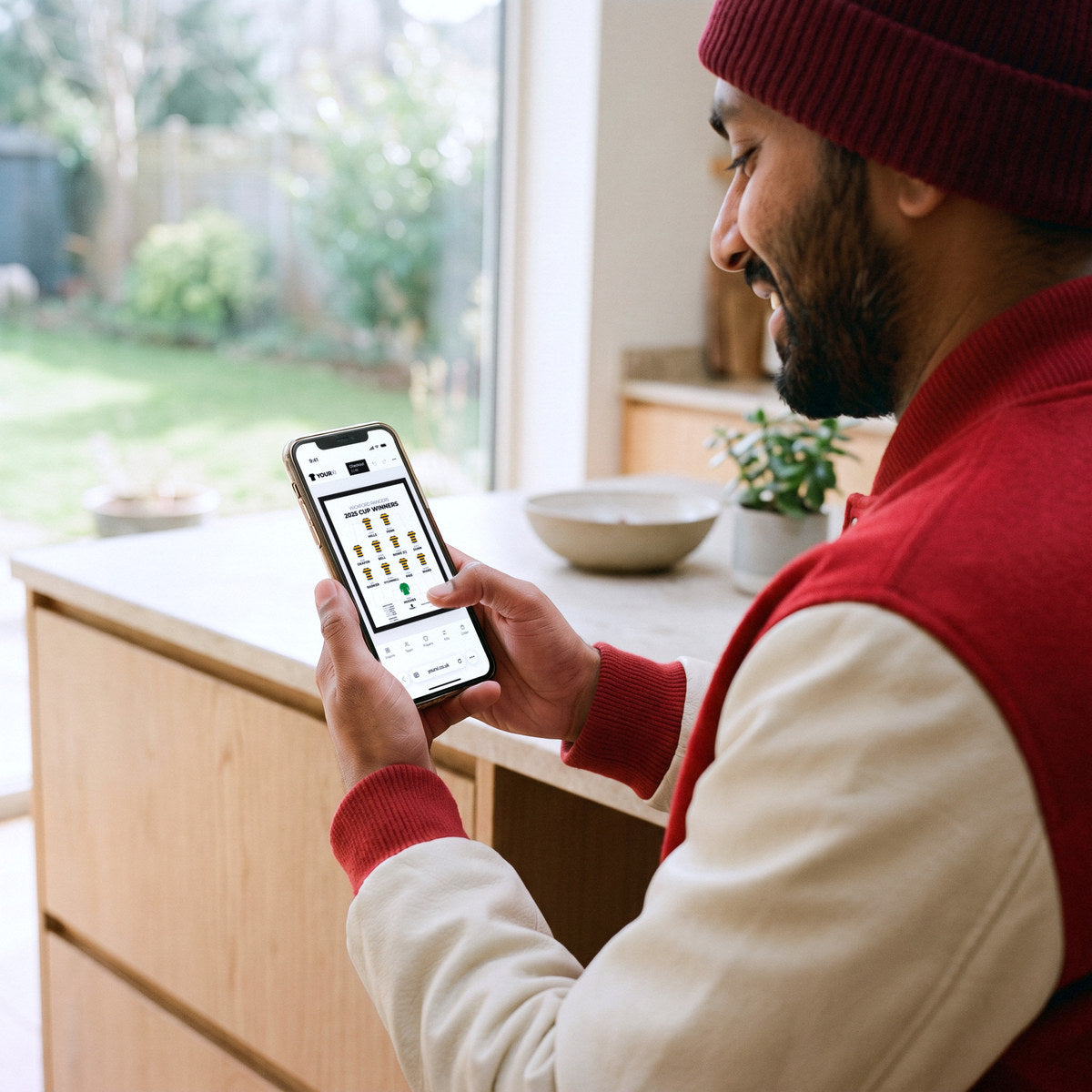 A fan in a red varsity jacket building his XI on his phone at the kitchen island